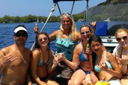 Group of people in swimwear posing on a boat with ocean and trees in background.