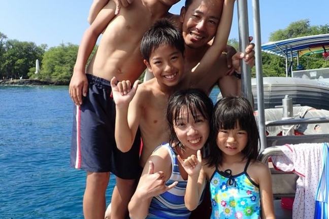 Family of five smiling on a boat by the water on a sunny day.