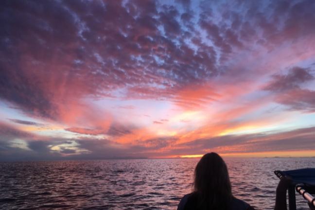 Person on a boat silhouetted against a vibrant sunset over the ocean.