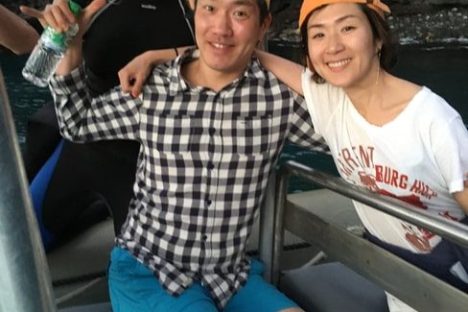 Three people on a boat pose with sushi, wearing casual clothes and hats.