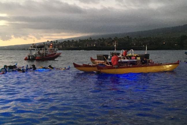 Snorkelers in water near boats at dusk under cloudy sky.