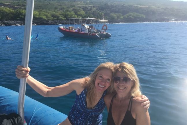 Two women smiling on a boat with an ocean view and another boat in the background.